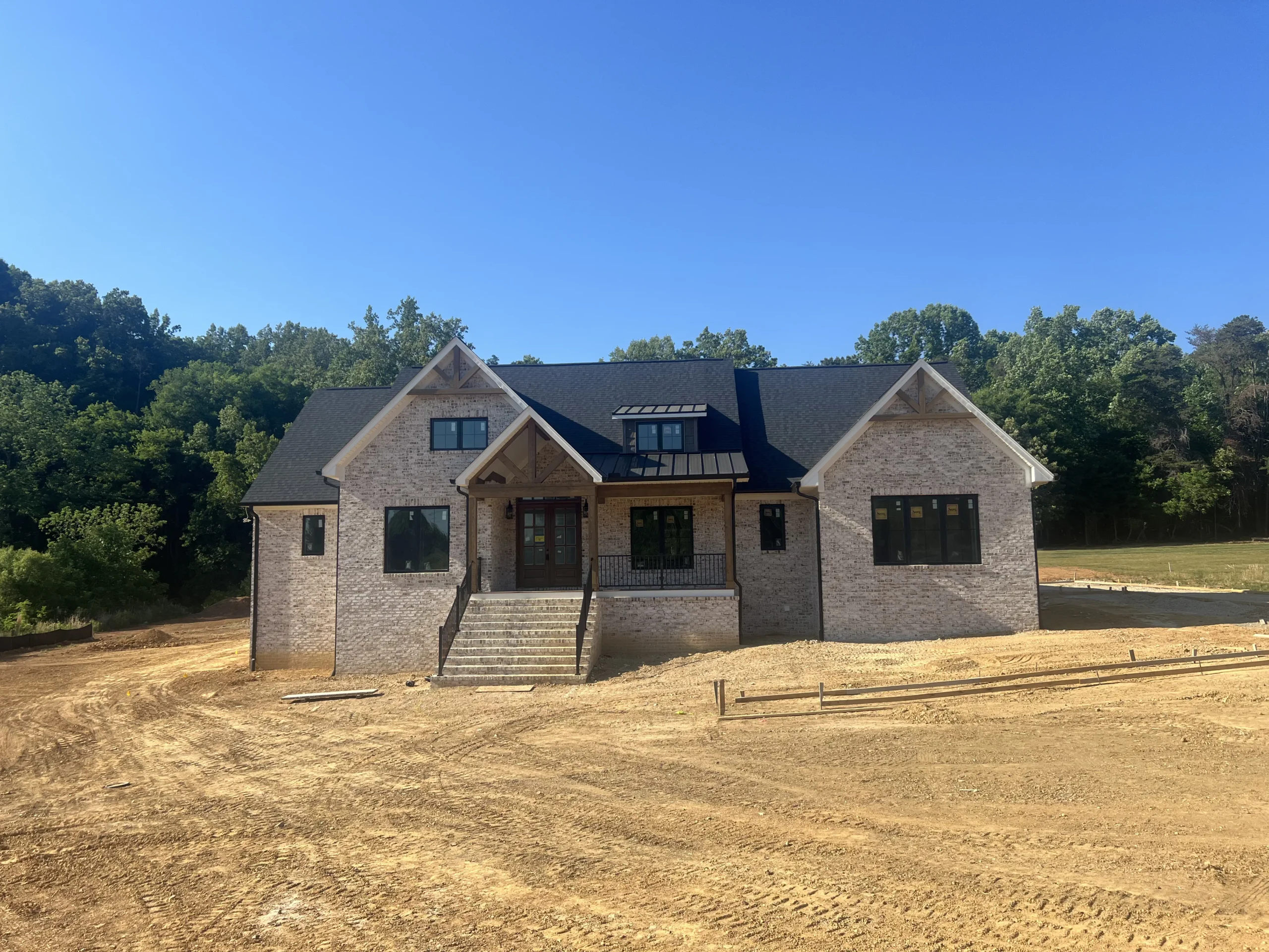 Front view of a custom brick home under construction by Lakenridge Homes in Beroth Farms, Pfafftown, NC, featuring a covered front porch, timber accents, and a spacious one-acre homesite.